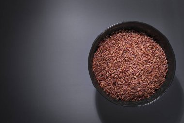 Koyu bir masaya bir kase kırmızı pirinç konur. Çiğ pirinç siyah kâseye yayılır..