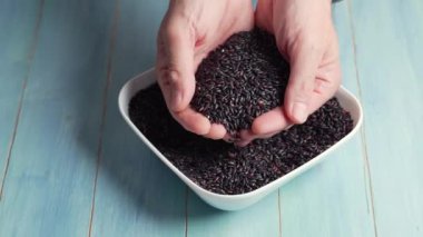 Çiğ siyah pirinç bir adamın ellerinden mavi arka planda beyaz bir kaseye düşer..