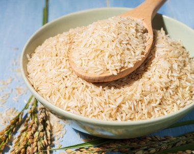 Bir kase kahverengi pirinç, bir kaşık dolusu pirincin ve pirincin yanındaki mavi masaya konur. Çiğ pirinç kaseye yayılır ve kaşık çiğ pirinç ile doldurulur.