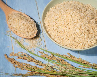 Bir kase kahverengi pirinç, bir kaşık dolusu pirincin yanında mavi bir masanın üzerine konur. Kase çiğ pirinç ile doludur. Kahverengi pirinç kaseye yayılır..