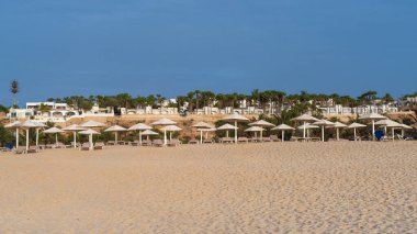 Beach scene with several umbrellas and beach chairs. The umbrellas are white and the chairs are beige. Scene is relaxed and peaceful, background luxury resort, Boa Vista,Cape verde
