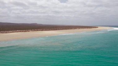 Aerial footage of Santa Monica Beach,showcasing endless white sand, turquoise waves, and a pristine,background volcanic mountain and desert,Boa Vista, Cape Verde.