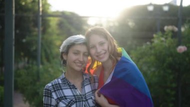 Gökkuşağı bayraklarıyla sarılan iki genç kadın.