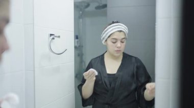 Aynada pamuk pedlerle yüzünü temizleyen odaklanmış bir kadın. Yüksek kalite 4k görüntü