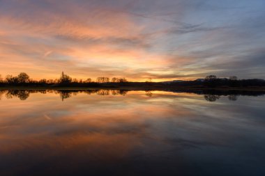 Gün batımında suya yansıyan ağaçlar. Kış manzarası kırmızı ve turuncu gökyüzü. Bas-Rhin, Alsace, Grand Est, Fransa, Avrupa.