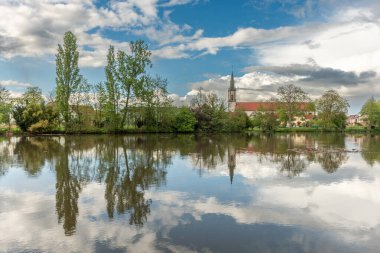 Huttenheim village reflected in a natural tree-lined river in spring. Bas Rhin, Alsace, France, Europe