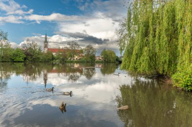 Huttenheim village reflected in a natural tree-lined river in spring. Bas Rhin, Alsace, France, Europe