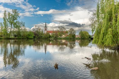 Huttenheim village reflected in a natural tree-lined river in spring. Bas Rhin, Alsace, France, Europe