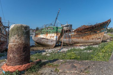 Sahilde büyük bir beton direğin yanında paslı bir tekne oturuyor. Tekne eski ve terk edilmiş. Sahne sessiz ve huzurlu.