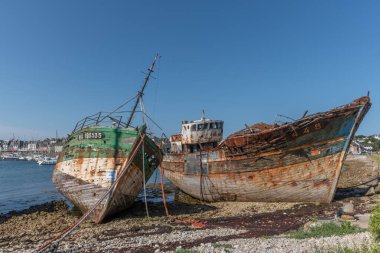 Sahilde büyük bir beton direğin yanında paslı bir tekne oturuyor. Tekne eski ve terk edilmiş. Sahne sessiz ve huzurlu.