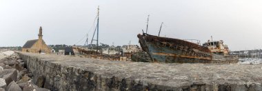 Sahilde büyük bir beton direğin yanında paslı bir tekne oturuyor. Tekne eski ve terk edilmiş. Sahne sessiz ve huzurlu.