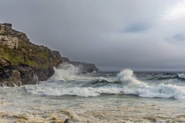 Okyanus dalgalı ve gökyüzü bulutlu. Dalgalar kayalara çarpıyor. Sahne yoğun ve dramatik.
