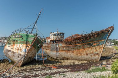 Sahilde büyük bir beton direğin yanında paslı bir tekne oturuyor. Tekne eski ve terk edilmiş. Sahne sessiz ve huzurlu.