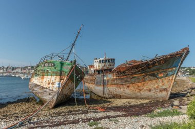 Sahilde büyük bir beton direğin yanında paslı bir tekne oturuyor. Tekne eski ve terk edilmiş. Sahne sessiz ve huzurlu.