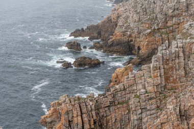 Kayalık bir uçurumu ve bir su kütlesi olan kayalık bir kıyı şeridi. Su dalgalı ve kayalar turuncu. Camaret, Crozon, Finistere, Bretagne, Fransa, Avrupa.