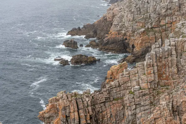 Kayalık bir uçurumu ve bir su kütlesi olan kayalık bir kıyı şeridi. Su dalgalı ve kayalar turuncu. Camaret, Crozon, Finistere, Bretagne, Fransa, Avrupa.