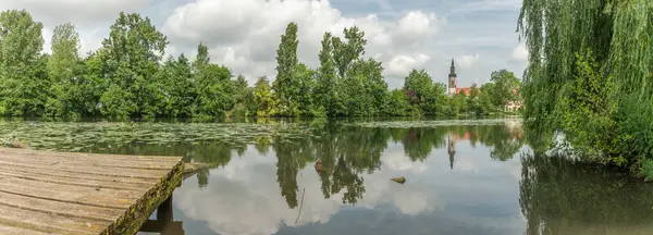 Arka planda ağaç olan bir göl. Su sakin ve hareketsiz. Arka planda bir bina var. Huttenheim, Bas rhin, Alsace, grand est, France, Europe.