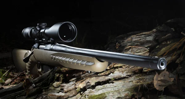 Scope on a bolt action hunting rifle on a log in a dark woodland