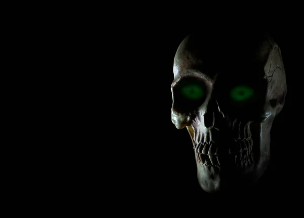 Green eyes glowing on a human skull with dark background