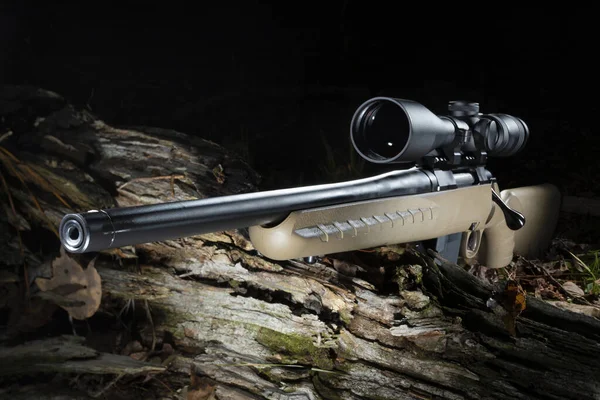 Bolt action rifle with a scope on a log in a dark forest
