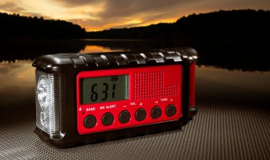 Saatli kırmızı hava radyosu ve gölün arkasında yükselen güneş ışığı.