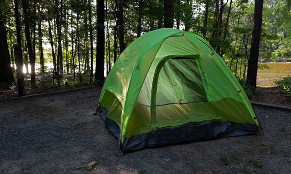 Light reflecting of a lake's water behind a tent in a tree lined campsite.