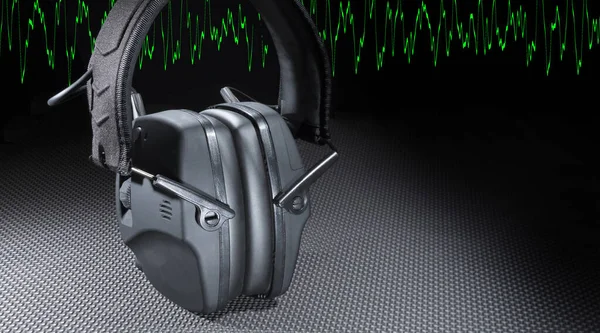 Copy space next to electronic headphones to protect hearing with a green sine wave running behind