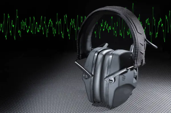 Copy space next to electronic headphones to protect hearing with a green sine wave running behind