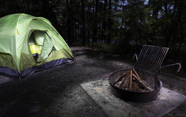 Firewood in a fire ring next to a pitched tent in a dark campsite
