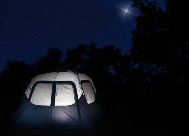 İçeriden aydınlatılmış büyük bir çadır. Gökyüzündeki en parlak yıldızın parladığı bir orman siluetinin yanında..