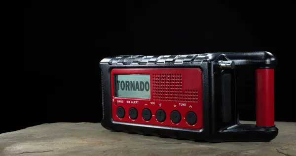 Room for text next to a red and black weather radio that runs on batteries with solar and hand crank backup showing a tornado watch on its LCD screen.