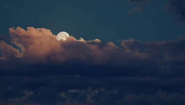 Sarı, mavi ve turuncu bulutlar gecenin erken saatlerinde yükselen ayı hafifçe karalıyor..