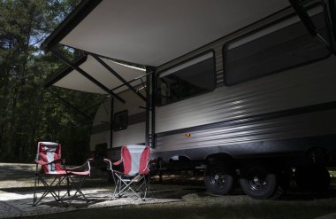 Kamp sandalyeleri ve tenteli bir karavan. Bir yaz kampında bir sürü ağaç var.. 
