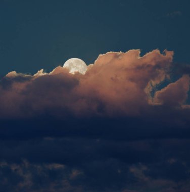 Aşağıda turuncu ve mavi bulutlarla yükselen ay.