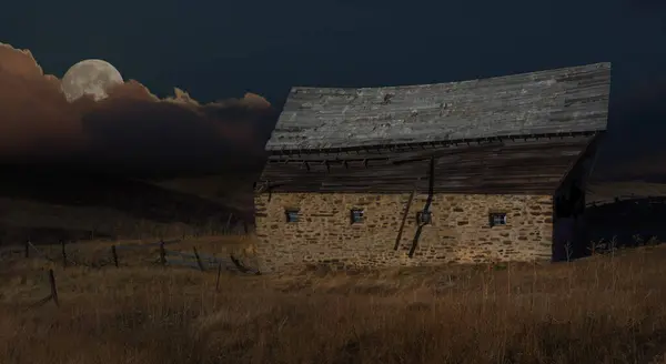 stock image Full moon rising above clouds on the horizon in hilly country over an old abandoned barn shortly after the sun has set.