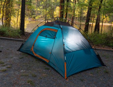Bir gölün yanındaki orman kamp alanında kurulmuş küçük mavi bir sırt çantası çadırı açık hava yaşam tarzı macerasına başlamak için ideal bir yerdir..