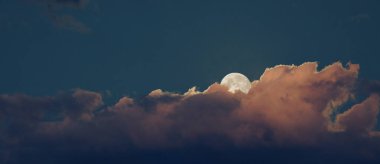 Arkadan yükselen parlak beyaz dolunay ve arka plan için turuncu bulutlar..