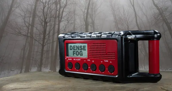 stock image LCD screen on a weather radio showing the dense fog warning issued by the weather service with trees in a thick forest shrouded in fog.