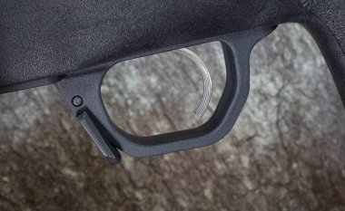 Polimer siyah tüfek tetiğiyle doldurulmuş ve yakın mesafeden tetik tetikleyicisi görülmüş, şarjör serbest bırakılmış ve arka plan olarak büyük bir kaya kullanılmış..