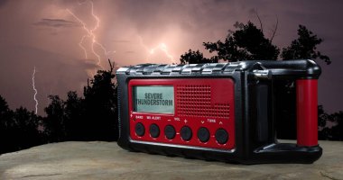 Kırmızı pille çalışan hava durumu radyosunun arkasında yıldırım çarpıyor. Şiddetli bir fırtına uyarısı LCD ekranında açıkça görülüyor..