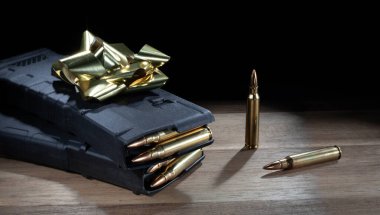 Dolu yüksek kapasiteli AR-15 şarjörleri, ahşap bir masanın üzerinde duran altın bir fiyonk hediye olarak..