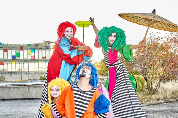 stock image Group of face-painted performers in colorful clown costumes and wigs juggling and dancing on stilts during the parade in the city park.