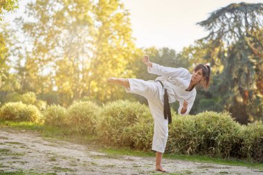 Siyah kuşaklı kadın karate dövüşçüsü doğada tekme pratiği yapıyor. Spor ve dövüş sanatları konsepti.