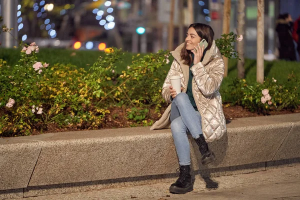 コーヒーカップで屋外に座っている間 女性は電話で話して笑顔 冬と技術の概念 — ストック写真