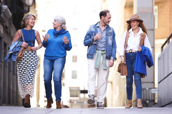 4人のアクティブな高齢者は 都会の風景を探索しながら 静かな街をゆっくりと散歩したり おしゃべりしたり笑ったりします — ストック写真
