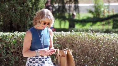 Bankta otururken telefonla mesajlaşan son sınıf öğrencisi kadın: 60 'lı yaşlarda son sınıf öğrencisi bir kadın cep telefonuyla mesajlaşırken bankta oturuyor, açık havada temiz havanın tadını çıkarıyor..