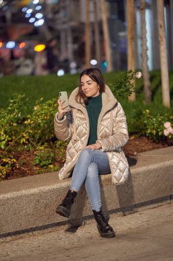 Kadın dışarıda otururken cep telefonunu tutuyor ve kullanıyor. Teknoloji konsepti.