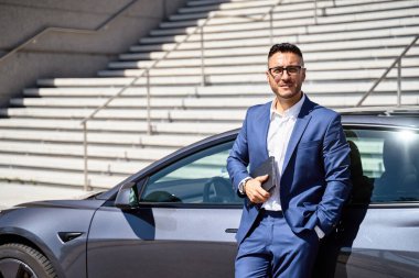 Gülümseyen yönetici arabaya yaslanıyor, tableti tutuyor ve kameraya bakıyor. İş ve Teknoloji Konsepti