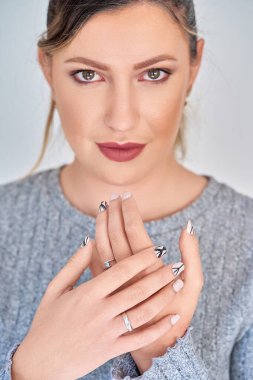 Manikür tırnaklarıyla ellerini gösterirken kameraya bakan şık bir kadın. Manikür ve güzellik konsepti.