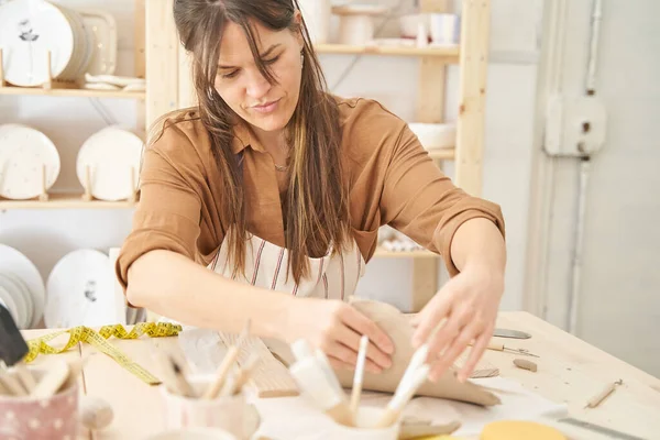 Woman painting and decorating a pottery in a ceramic workshop. Craft, art and hobbies concept.